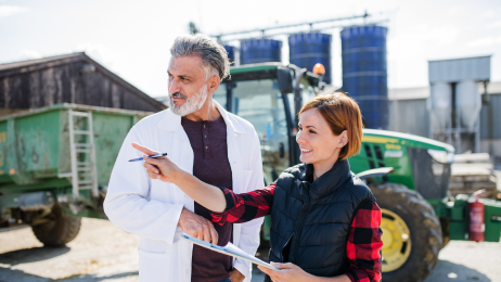 man and woman holding a clipboard infront of a tractor